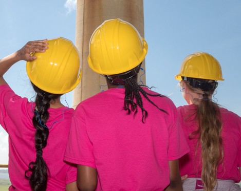 Three girls in hard hats looking out into the distance